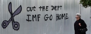 A woman walks past a graffiti that reads "Cut the debt, IMF go home" in Athens